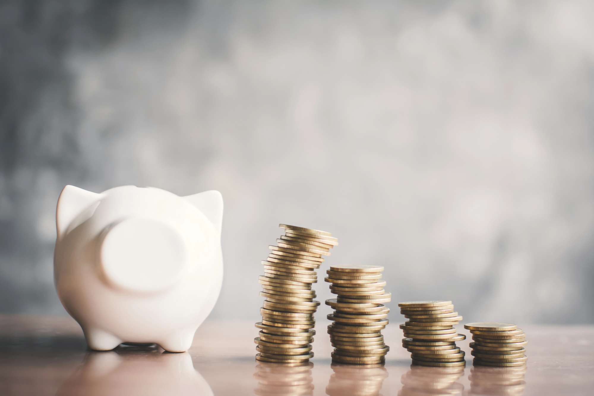 Biała świnka skarbonka i rosnące stosy monet, symbolizujące aprecjację wartości pieniądza i oszczędzania, na tle rozmytego tła.