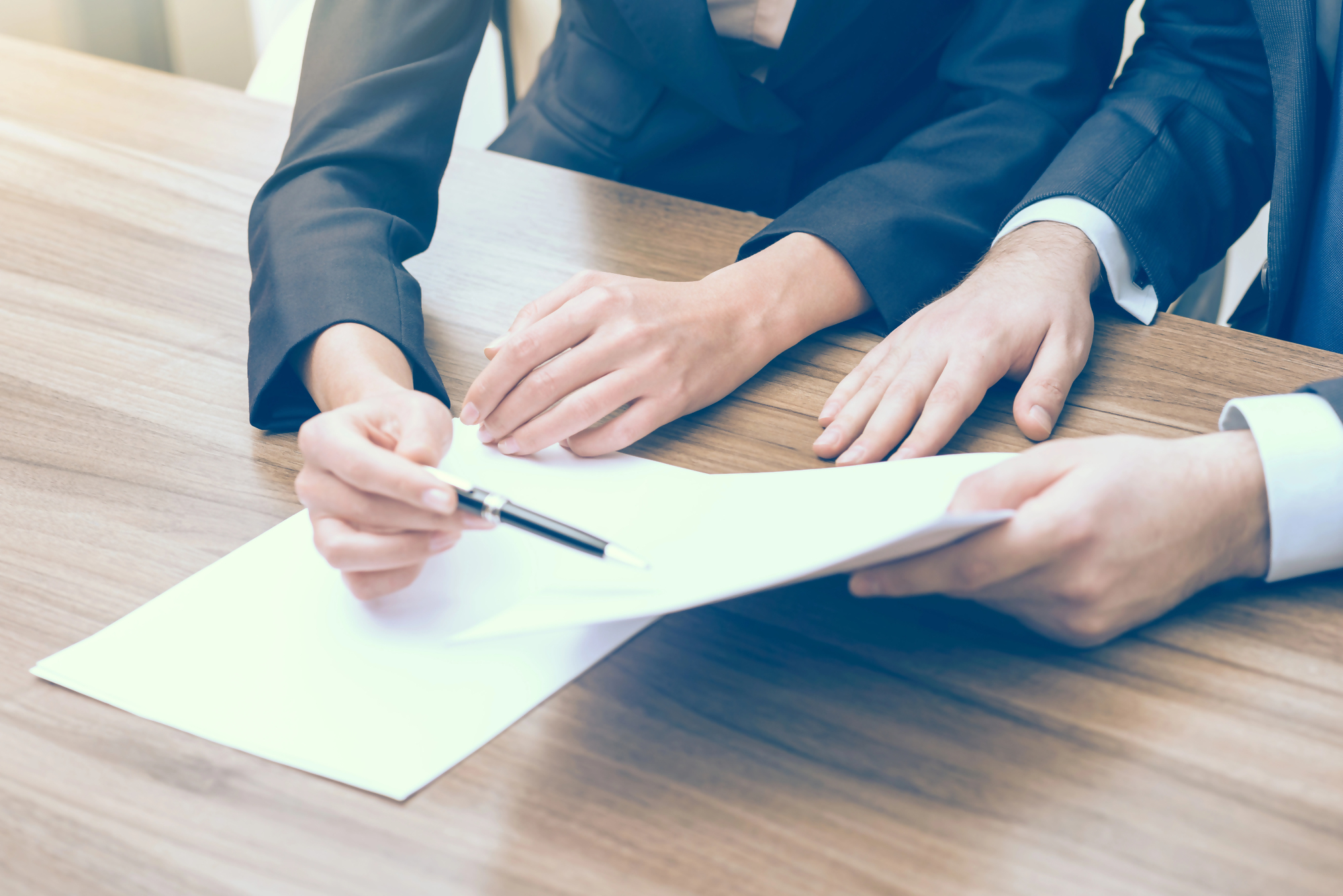 Dwie osoby w garniturach omawiają dokumenty związane z kredytem hipotecznym, koncentrując się na temacie minimalna kwota kredytu hipotecznego, siedząc przy drewnianym stole.