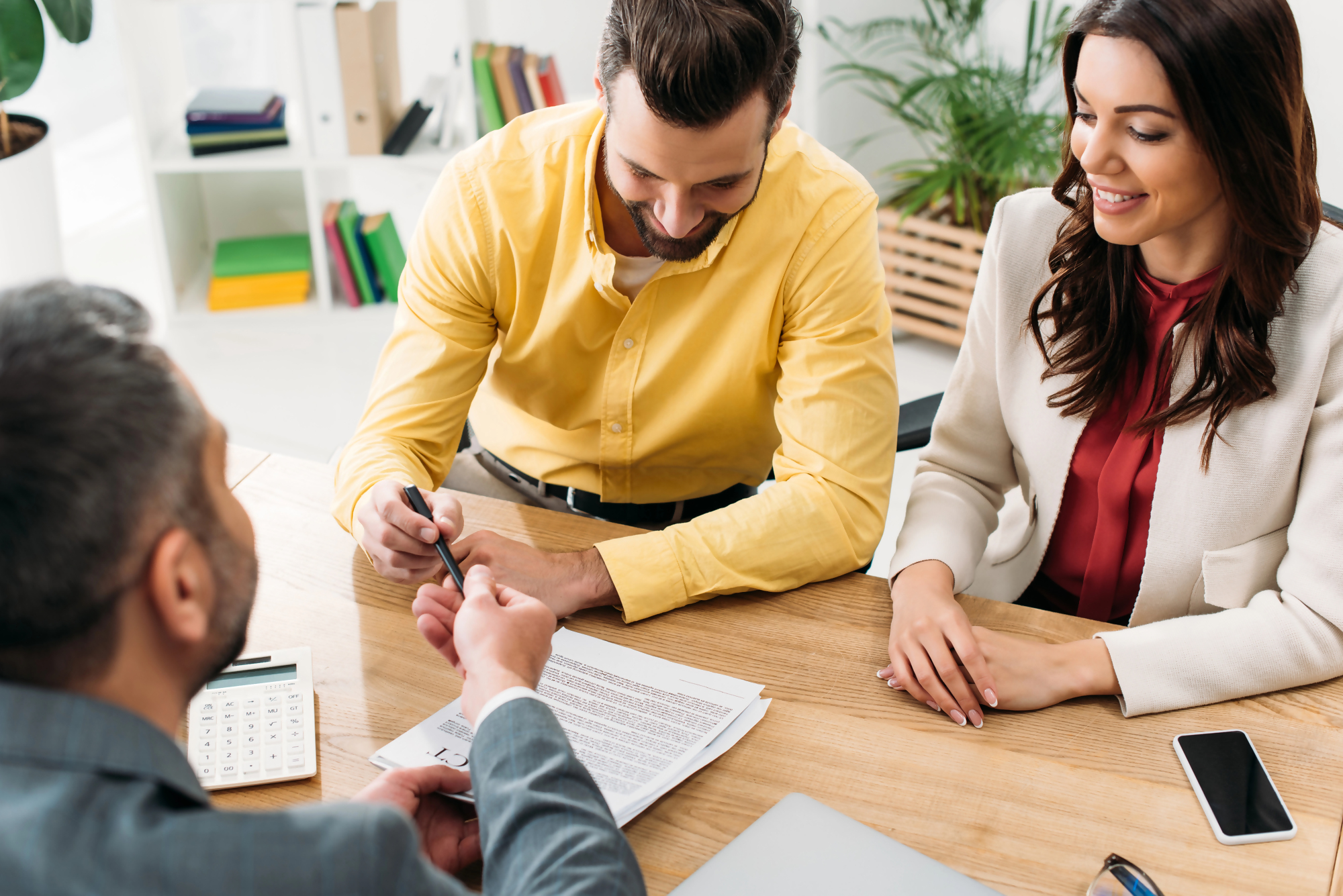 Spotkanie pary z doradcą finansowym przy biurku, podpisywanie dokumentów dotyczących finansowania i omawiana jest minimalna kwota kredytu hipotecznego.