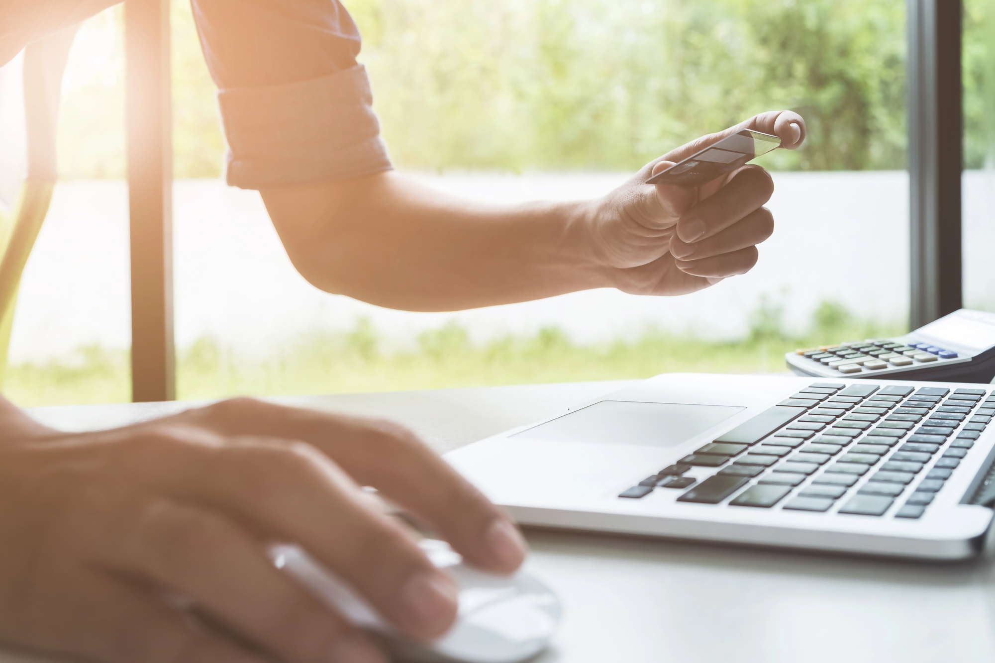 Osoba pracująca przy laptopie, używająca karty płatniczej oraz kalkulatora, przedstawiająca analizę finansową i obliczanie wartości dyskonto w biznesie lub podczas zakupów online.