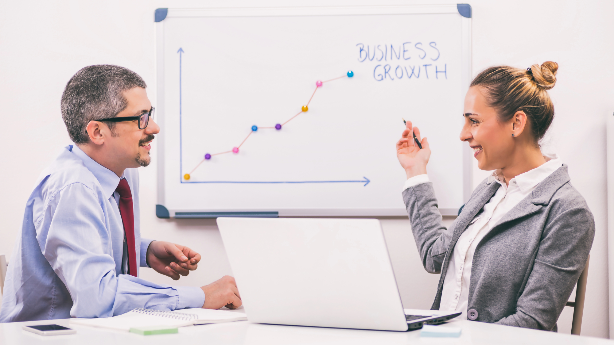 Biometria w biznesie – dwie osoby omawiają strategie wzrostu biznesowego przy wykresie na tablicy, wykorzystując nowoczesne rozwiązania z zakresu biometrii w przedsiębiorstwie.