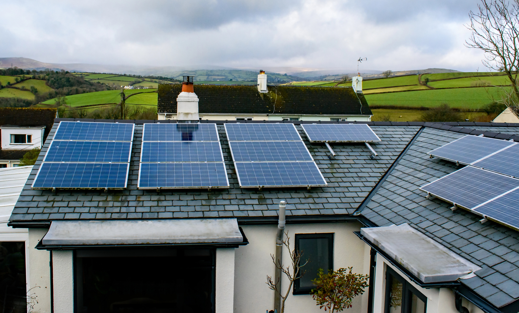 Sprzedaż mieszkania z kredytem – dom jednorodzinny z panelami fotowoltaicznymi na dachu, otoczony zielonym krajobrazem, pokazuje nowoczesne rozwiązania podczas sprzedaży nieruchomości objętej kredytem hipotecznym.