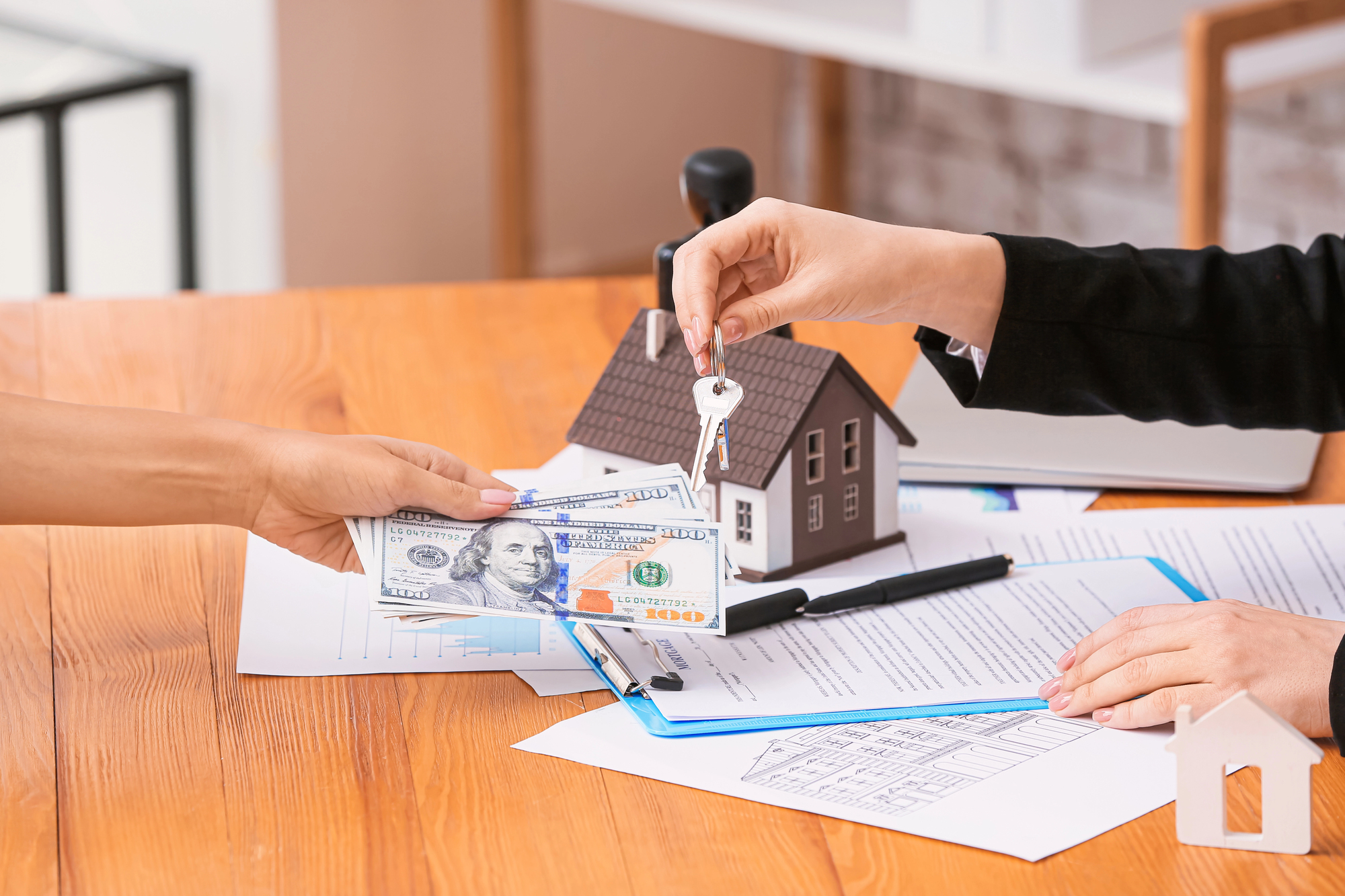 Co to jest lokata – na obrazku widoczne są dwie osoby przekazujące sobie klucze do domu oraz gotówkę, na biurku leżą dokumenty i makieta domu, co symbolizuje inwestowanie środków i poruszanie tematu co to jest lokata oraz bezpieczeństwo finansowe.