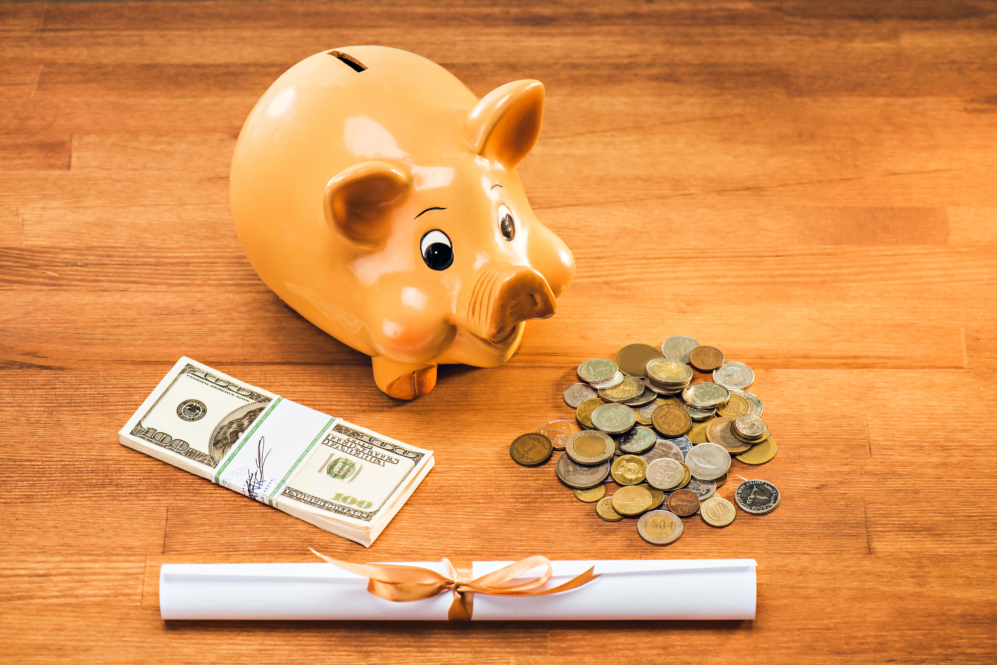 Sprzedaż mieszkania z kredytem – skarbonka świnka, gotówka w dolarach, monety i dokument na drewnianym stole, symbolizujące finanse i formalności związane z transakcją nieruchomości.