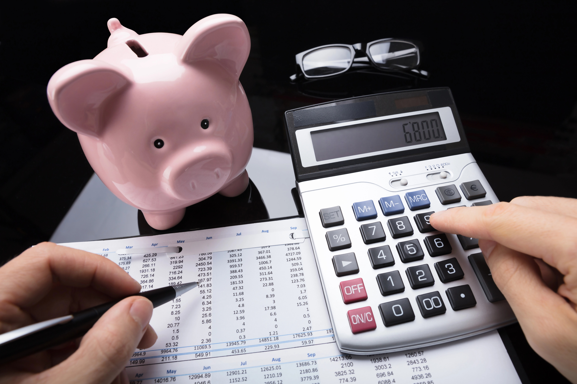 Osoba obliczająca raty leasingu przy użyciu kalkulatora i arkusza finansowego, obok znajduje się różowa skarbonka – koncepcja zarządzania finansami oraz korzyści leasingu.
