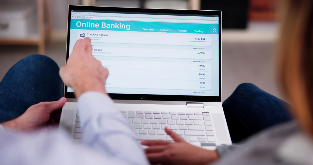 Osoby korzystające z bankowości internetowej na laptopie, ekran wyświetla panel konta online, zarządzanie finansami przez internet.