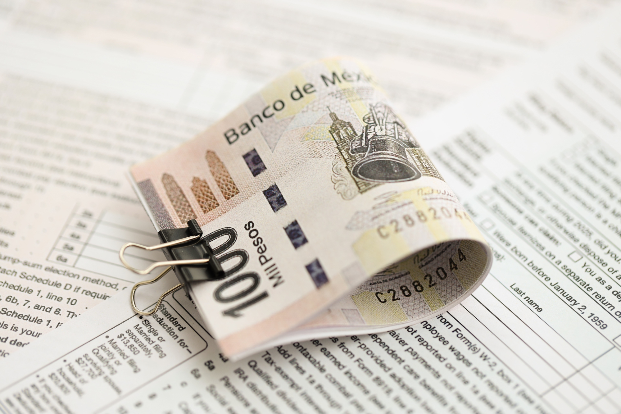 Co to jest lokata – zrolowany banknot 1000 pesos zabezpieczony spinaczem na tle dokumentów finansowych, symbolizujący inwestowanie pieniędzy na lokacie bankowej.