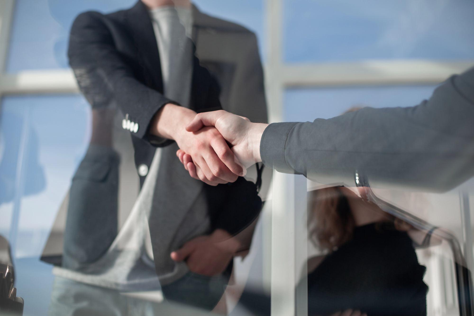 Lokata z funduszem co to – osoby w biurze podają sobie ręce na znak zawarcia umowy inwestycyjnej, symbolizując współpracę oraz wybór produktu finansowego łączącego lokatę bankową z funduszem inwestycyjnym.