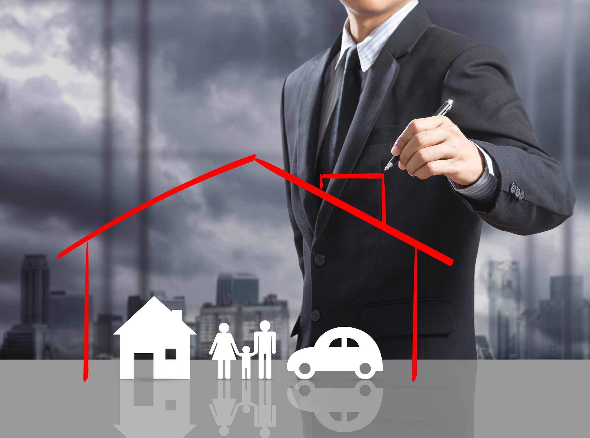 Brak ubezpieczenia mieszkania a kredyt hipoteczny – biznesmen rysuje linię dachu nad rodziną, domem i samochodem, symbolizującą ochronę, na tle miejskich budynków.