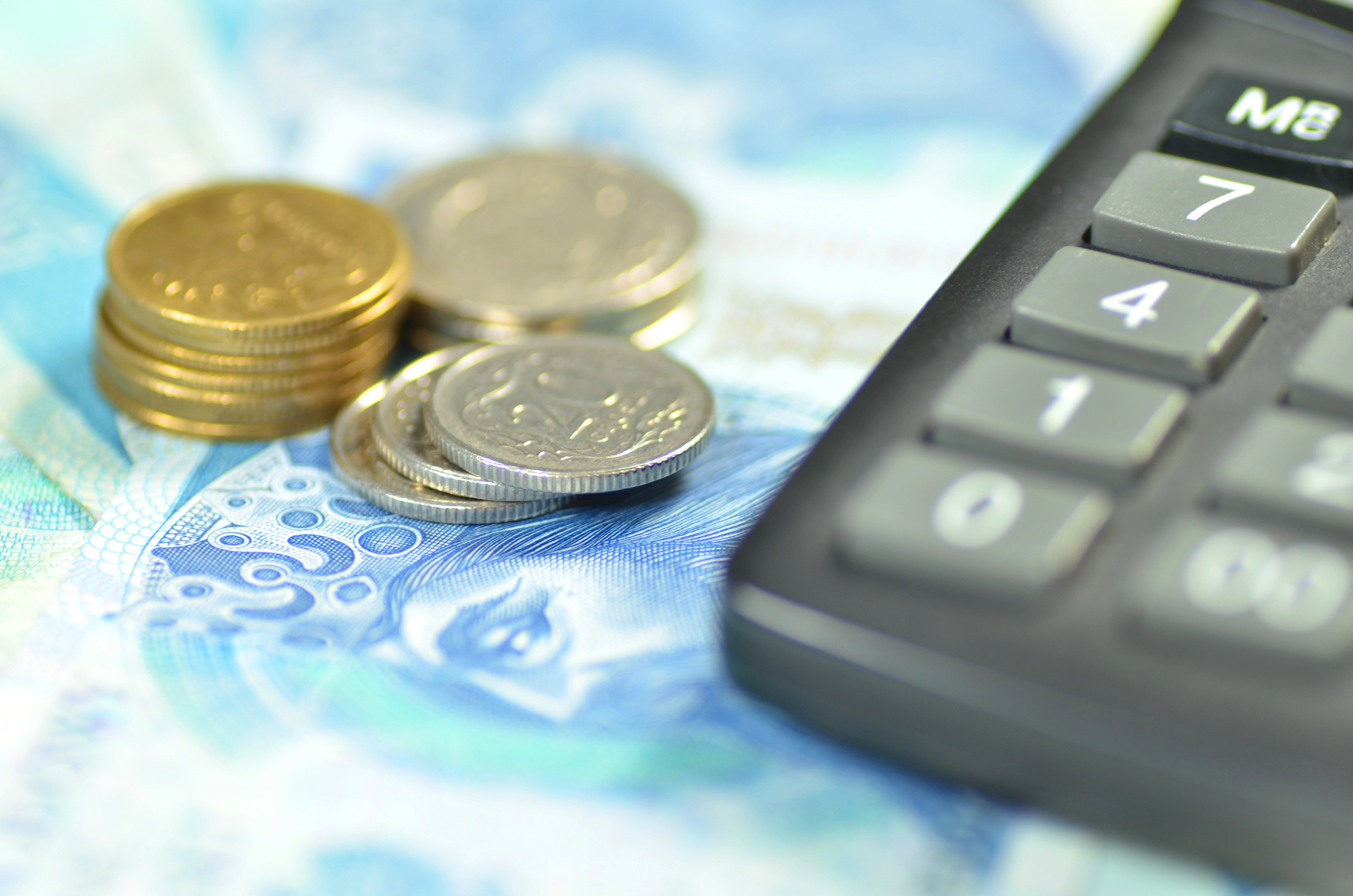 Monety, banknoty oraz kalkulator, symbolizujące obliczanie finansów oraz całkowita kwota kredytu podczas planowania zobowiązań kredytowych.