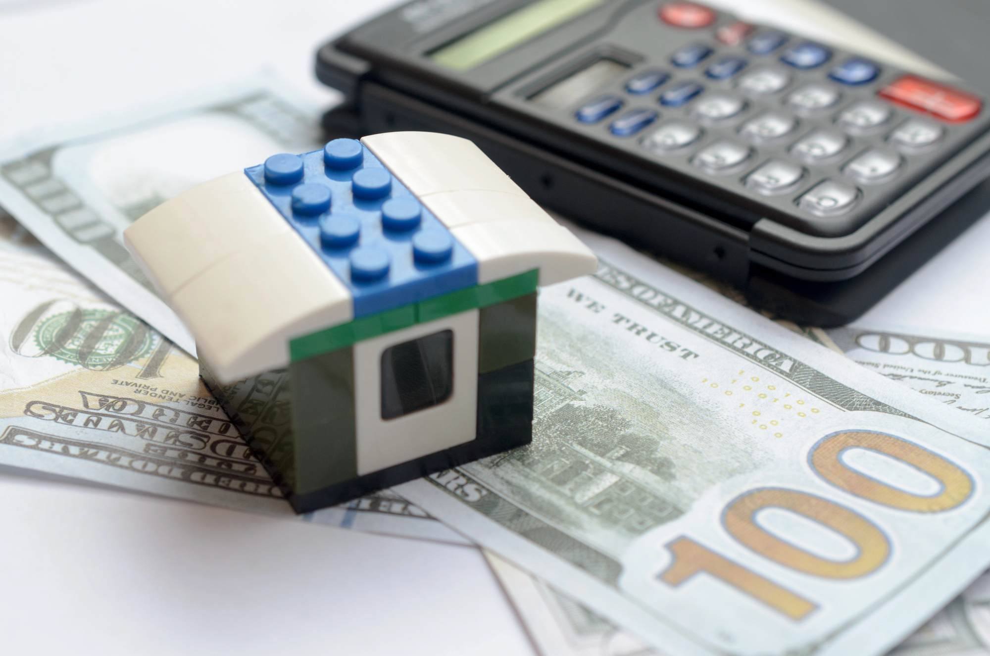 Brak ubezpieczenia mieszkania a kredyt hipoteczny – model domu z klocków na banknotach dolarowych obok kalkulatora, symbolizujący ryzyko finansowe związane z kredytem hipotecznym bez ubezpieczenia nieruchomości.