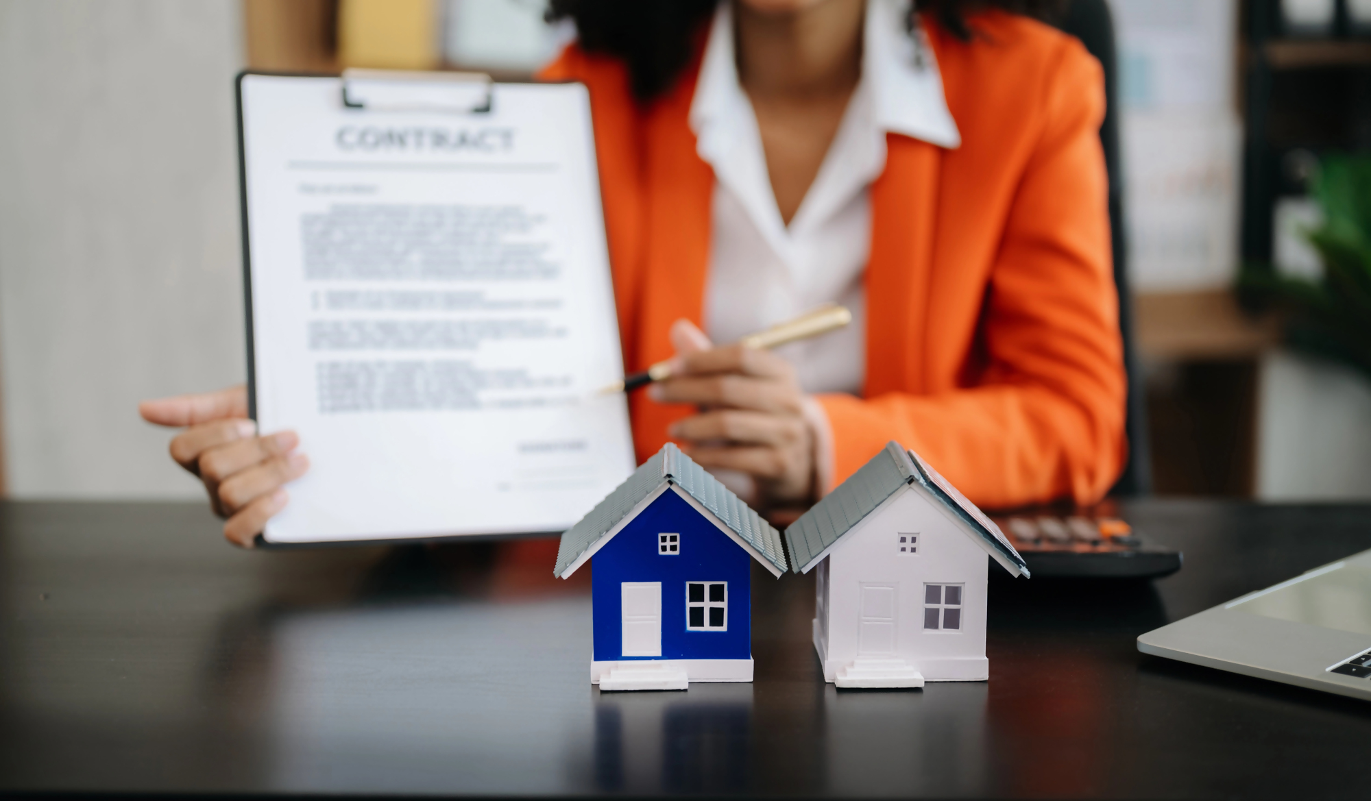 300 tys kredytu jaka rata – kobieta w garniturze prezentuje umowę kredytową, na biurku dwa modele domów jako symbol kredytu hipotecznego i wyliczenia raty.