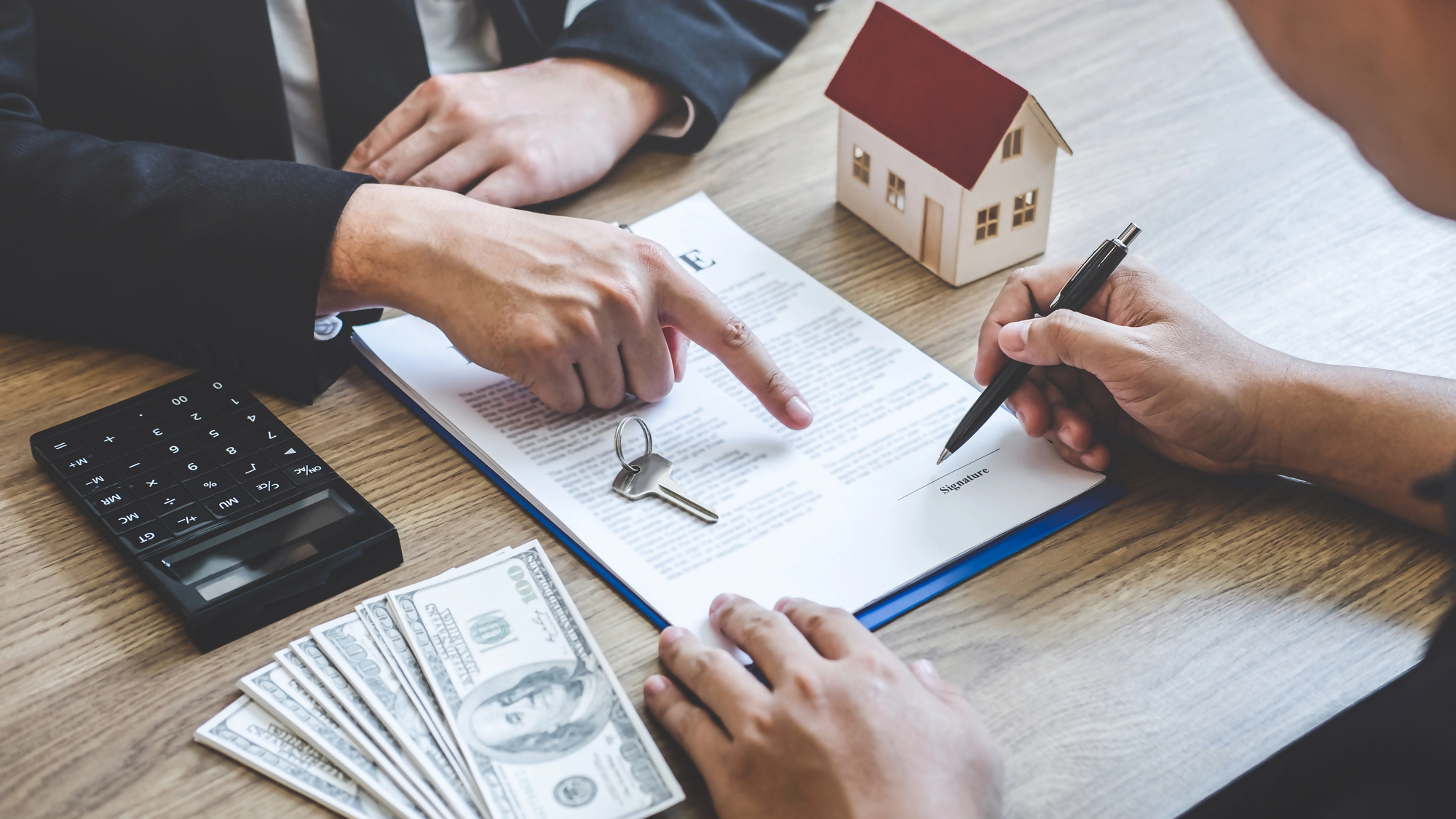 Ile się czeka na kredyt hipoteczny – spotkanie dwóch osób przy podpisywaniu umowy kredytowej, na stole kalkulator, pieniądze, klucze, dokumenty i model domu, symbolizujące proces uzyskania kredytu hipotecznego.