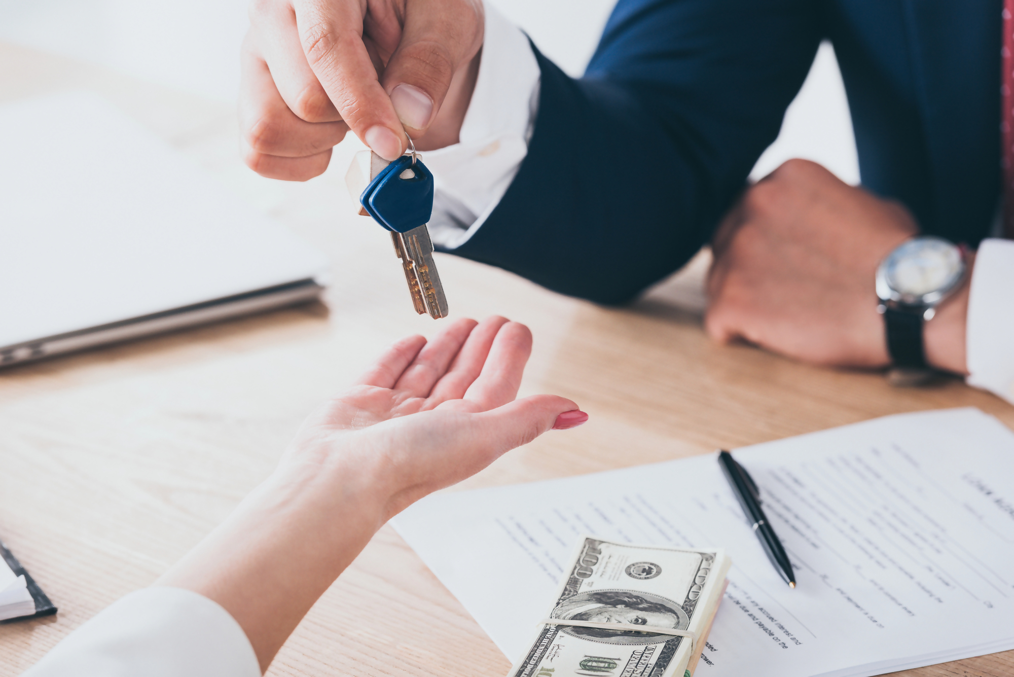 Kredyt 500 tys jaka rata – osoba przekazuje klucze do nieruchomości nad dokumentami i gotówką na stole, co symbolizuje zakup mieszkania lub domu na kredyt hipoteczny.