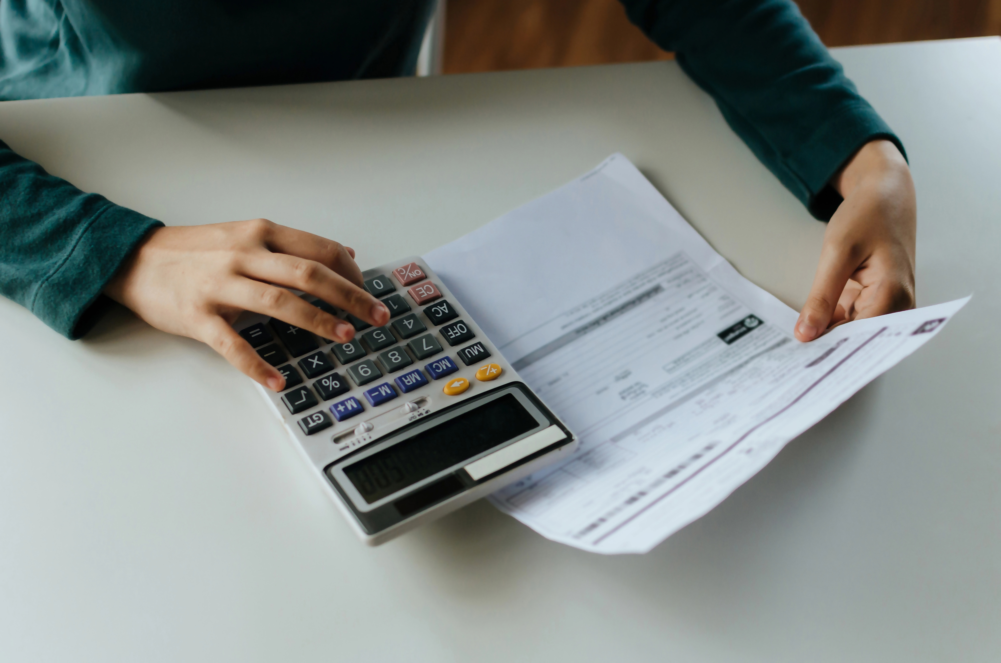 Osoba analizuje dokumenty finansowe i używa kalkulatora podczas rozważania sytuacji związanej z wypowiedzeniem umowy kredytu przez bank.