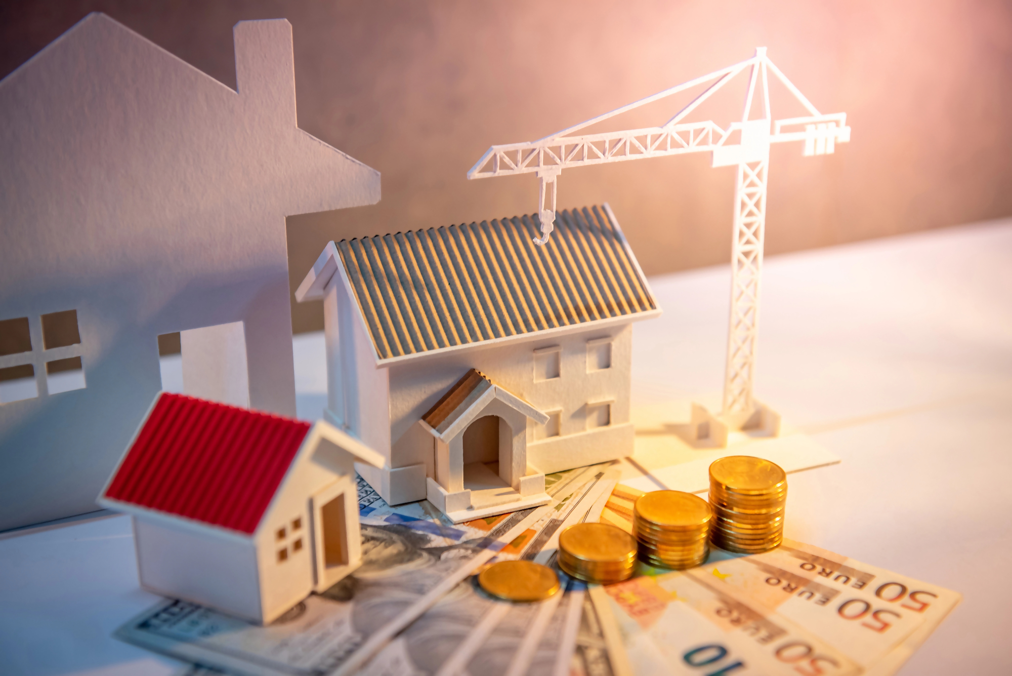 Kredyt 500 tys jaka rata – miniatury domów, żuraw budowlany, polskie banknoty i monety symbolizujące finansowanie budowy lub zakupu nieruchomości oraz wysokość raty kredytu hipotecznego.