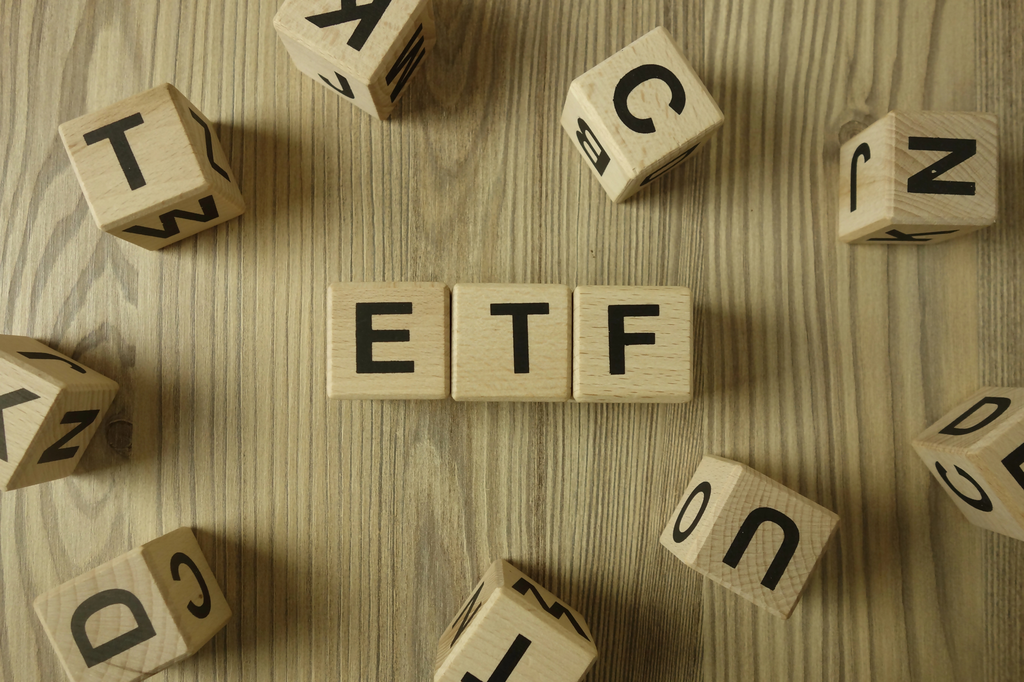 Drewniane klocki z literami układającymi się w napis "ETF" na drewnianym tle, symbolizujące fundusze ETF jako nowoczesny sposób inwestowania.