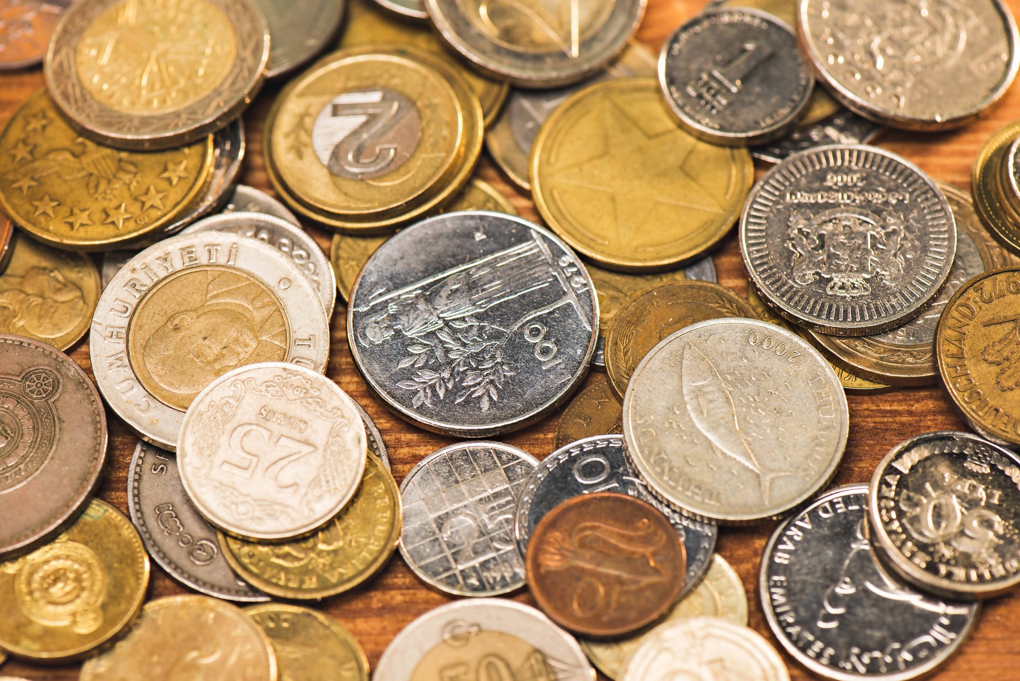 Czy warto trzymać oszczędności w euro – różne monety z różnych krajów na drewnianej powierzchni, symbolizujące rozważania na temat przechowywania oszczędności w obcej walucie, w tym euro.