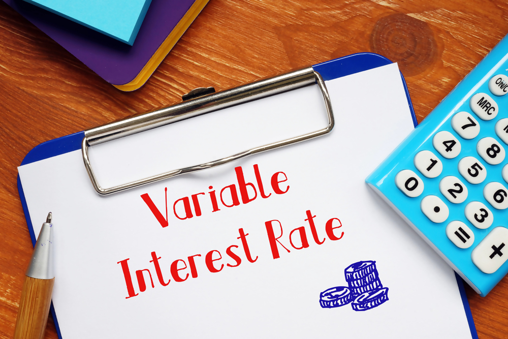 Notatka z napisem "Variable Interest Rate" na drewnianym biurku, obok kalkulator i długopis, koncepcja zmiennej stopy procentowej.