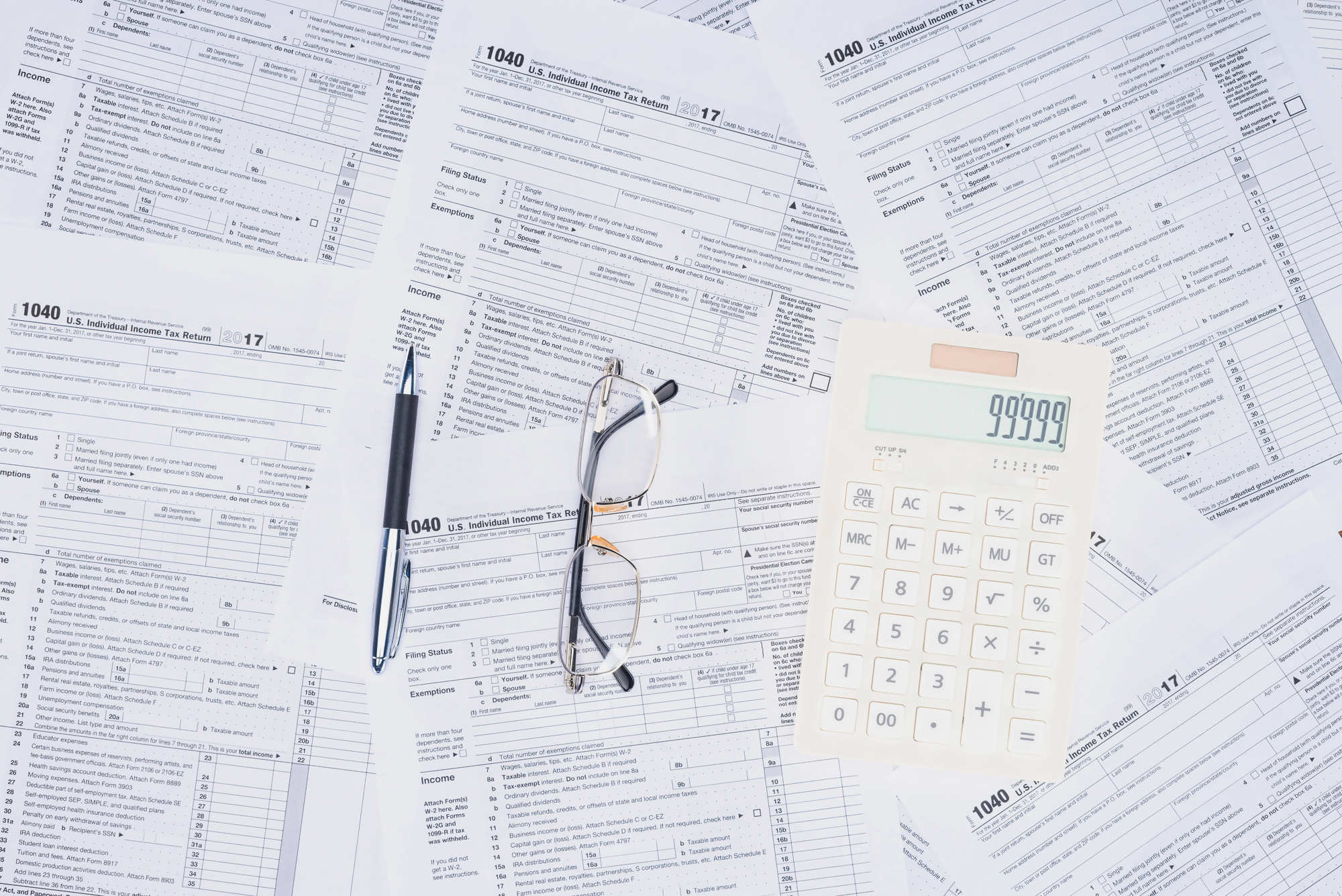 Monit dotyczący dokumentów podatkowych – na zdjęciu widoczne są formularze podatkowe, kalkulator, długopis oraz okulary, co symbolizuje przypomnienie o konieczności rozliczenia podatku.