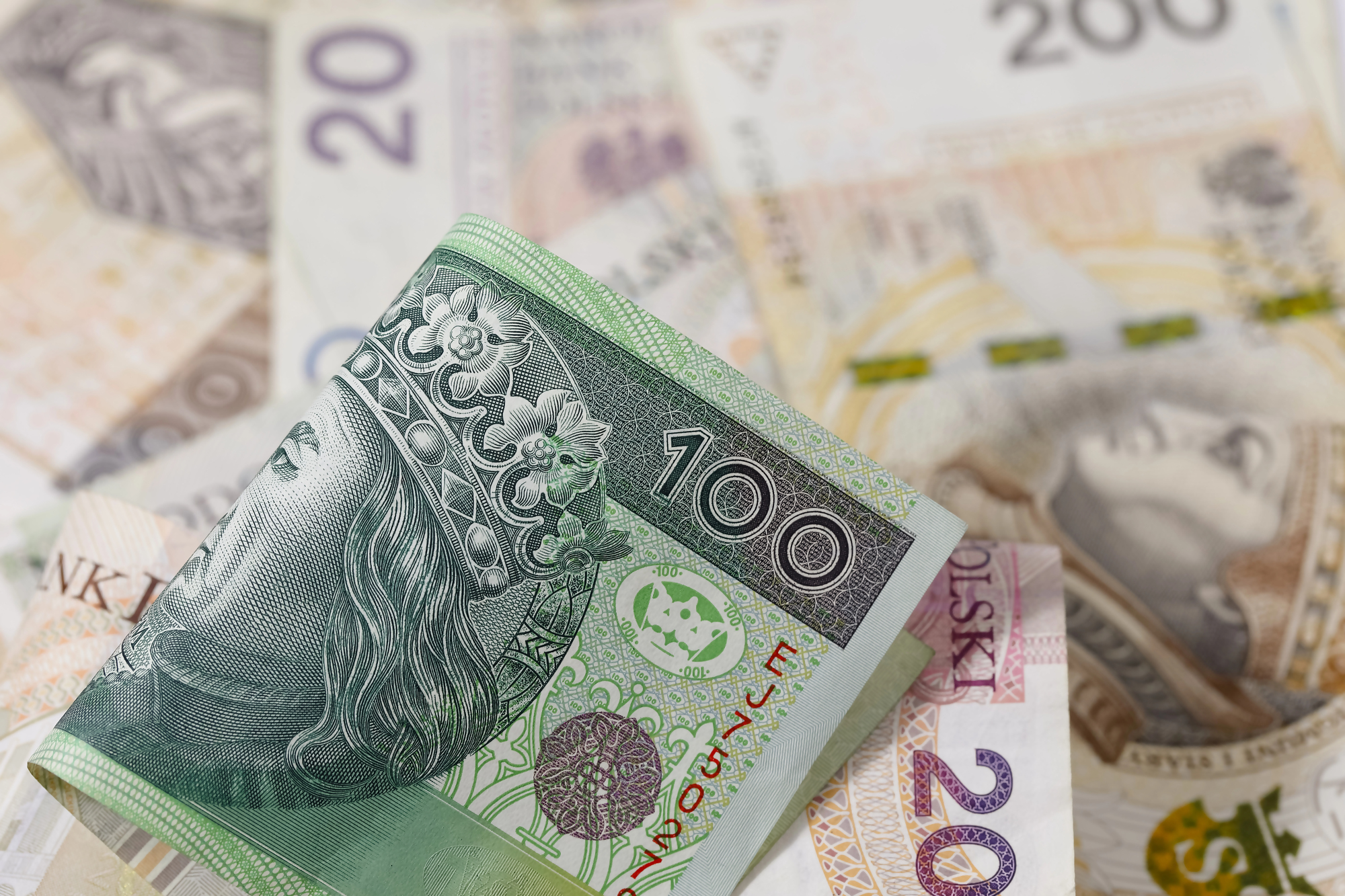 Wymiana zniszczonego banknotu – polskie banknoty o nominałach 100, 20 i 200 złotych ułożone na stole, zdjęcie ilustrujące proces wymiany uszkodzonych pieniędzy w banku.