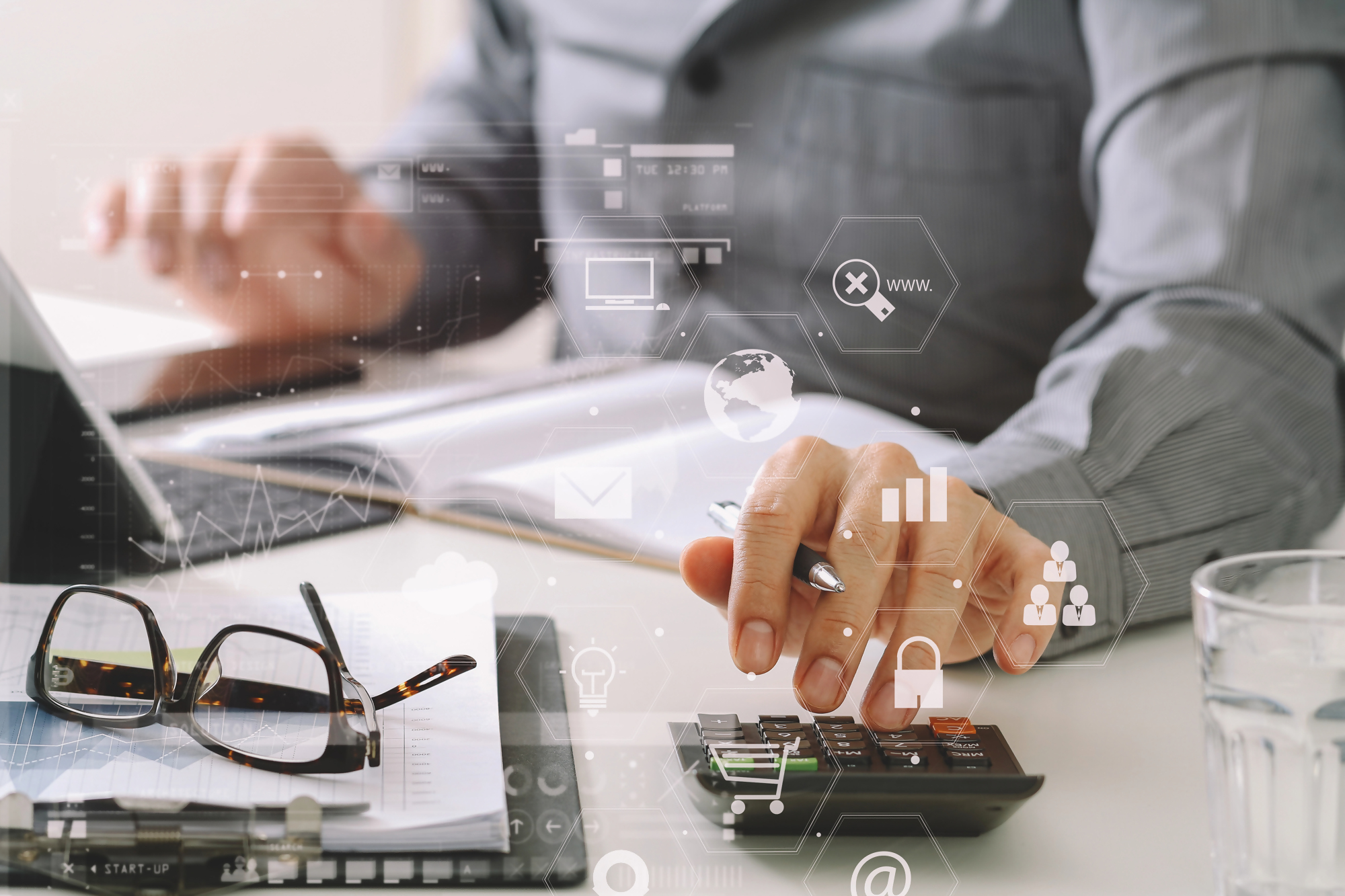 Biznesmen pracuje przy biurku, sporządzając aneks do umowy, obok laptop, notatnik, kalkulator i okulary – nowoczesne technologie wspierające zarządzanie dokumentami.