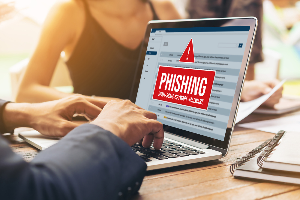 Osoba pracuje na laptopie, na ekranie wyświetla się ostrzeżenie przed phishingiem, spamem, oszustwem, spyware i malware w skrzynce e-mail.
