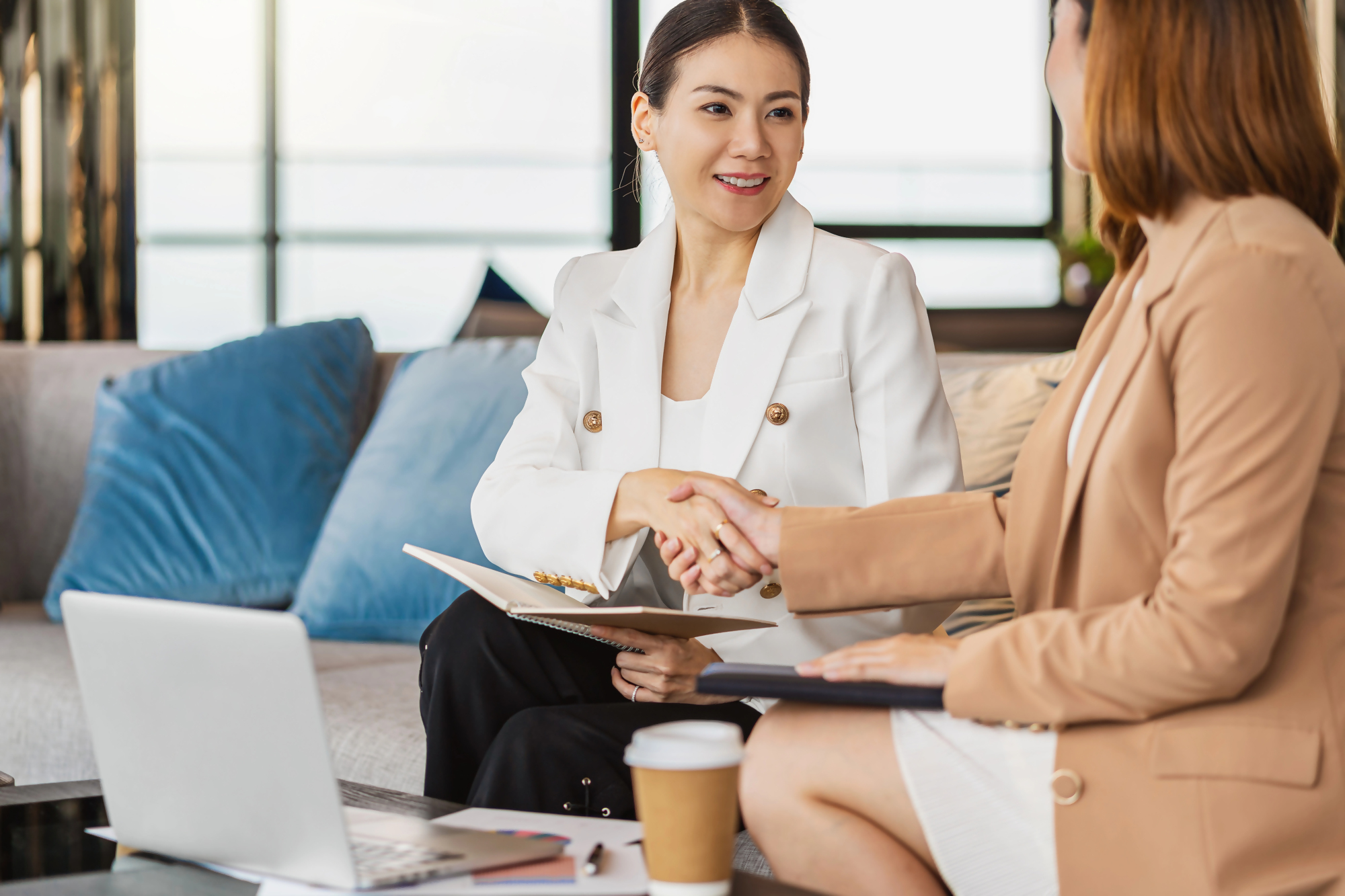 Dwie kobiety w biurze omawiające formalności związane z wypowiedzeniem umowy kredytu przez bank, podają sobie ręce na tle laptopa i dokumentów, ilustracja spotkania dotyczącego rozwiązania umowy kredytowej.