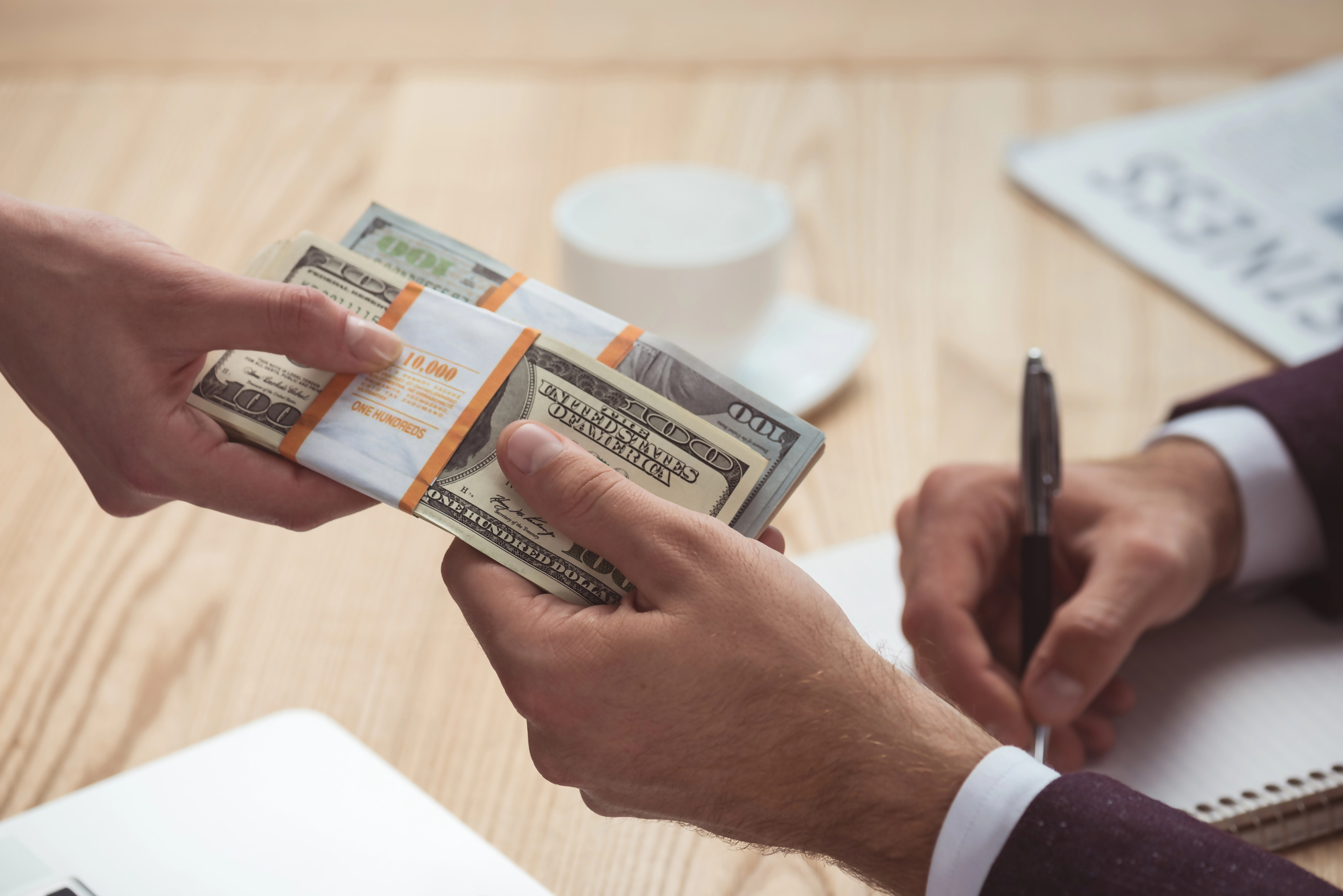 Deprecjacja waluty – przekazywanie pieniędzy w kontekście utraty wartości dolara amerykańskiego, dwie osoby wymieniają się gotówką przy biurku, symbolizując wpływ deprecjacji na transakcje finansowe.